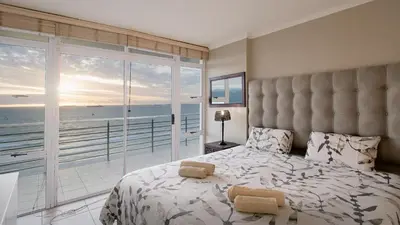 a bedroom with a large bed with a view of the ocean at The Waves Blouberg Beach Apartments in Bloubergstrand