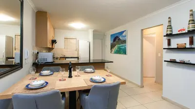 a kitchen with a wooden table and chairs in a room at The Waves Blouberg Beach Apartments in Bloubergstrand