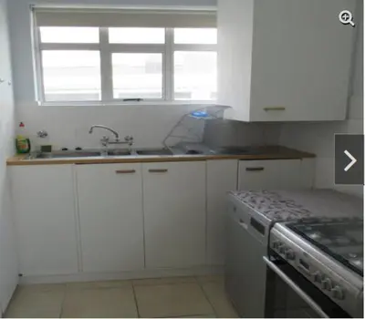 a kitchen with white cabinets and a sink and a stove at Romilly Beach Apartment in Strand