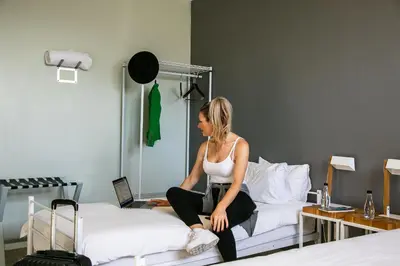 a woman sitting on a bed with a laptop at Zzzone Boutique Hostel in Hermanus