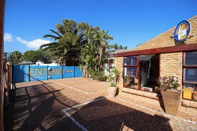 a building with a tennis court in front of it at Saltycrax Backpackers and Surf Hostel in Bloubergstrand