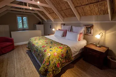a bedroom with a large bed and a red chair at Cook's Cottage in Franschhoek