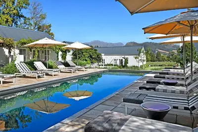 a swimming pool with chairs and umbrellas next to a house at Lavender Farm Boutique Guest House in Franschhoek
