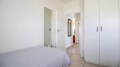 a white bedroom with a bed and a hallway at Greenways Strand Golf Beach C3 in Strand