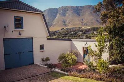a white house with a blue door and mountains in the background at Hemel en Aarde cottages in Hermanus