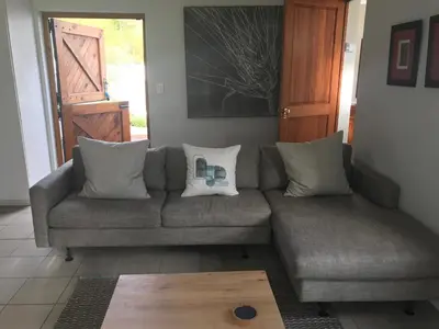 a living room with a gray couch with pillows at Hemel en Aarde cottages in Hermanus