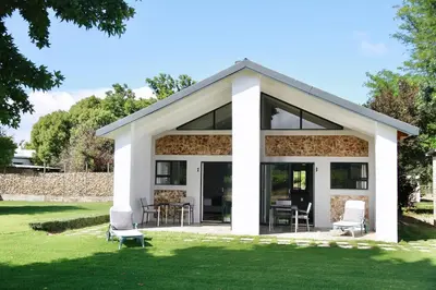 a house with glass doors and chairs on the grass at De Hoop Farm - Mountain View in Breerivier