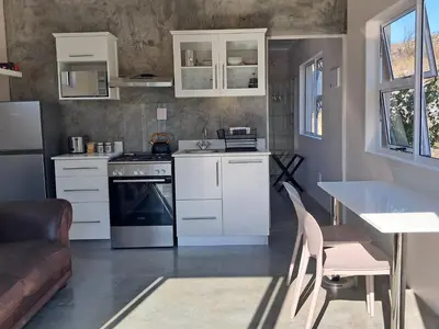 a kitchen with white cabinets and a table and chairs at Treyntjes Rivier Cottages in Caledon