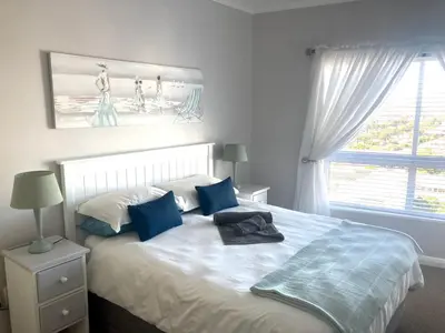 a bedroom with a bed with blue pillows and a window at Portico 606 in Bloubergstrand