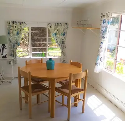 a wooden table and chairs in a room with windows at Weavers' Cottage in Gordonʼs Bay