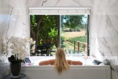a woman laying in a bath tub looking out a window at Alluvia Boutique Winery & Luxury Accommodation in Stellenbosch