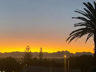 a sunset over the mountains with a palm tree at Four Palms Accommodation in Durbanville