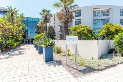 a sign in front of a building with palm trees at Lagoon Beach 237A by CTHA in Cape Town