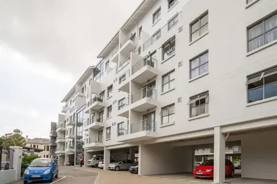 a white building with cars parked in a parking lot at The Rondebosch in Cape Town
