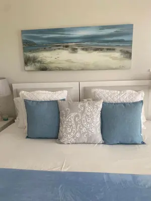 a bed with blue and white pillows and a painting at Shore's Edge Luxury Oceanfront Home in Hermanus