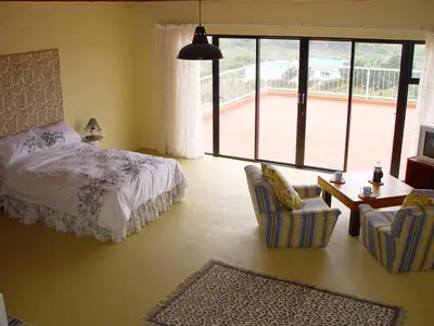 a bedroom with a bed and chairs and a large window at Jack's Seaview in Bettyʼs Bay