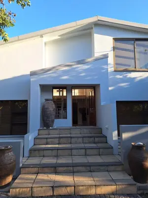 a white house with two large vases on the stairs at Arbeidsgenot Beach House in Hermanus