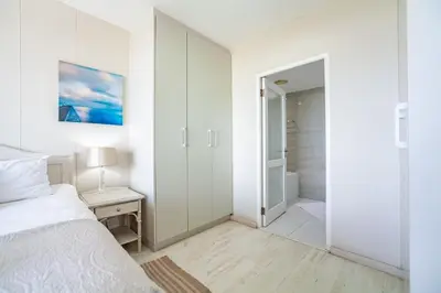 a white bedroom with a bed and a walk in shower at Luxury Private Beachfront 2 bedroom Dolphin Apartment, Blouberg, Cape Town in Bloubergstrand