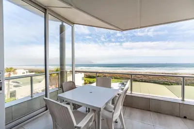 a dining room with a table and chairs and the ocean at Luxury Private Beachfront 2 bedroom Dolphin Apartment, Blouberg, Cape Town in Bloubergstrand