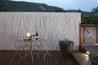 a table with two chairs and a bottle of wine on a deck at The Potting Shed Guest House in Hermanus