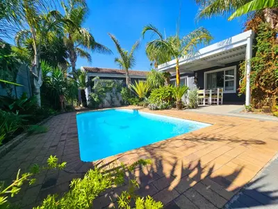 a swimming pool in front of a house with palm trees at Northern Vine Guesthouse B&B Self-catering in Brackenfell