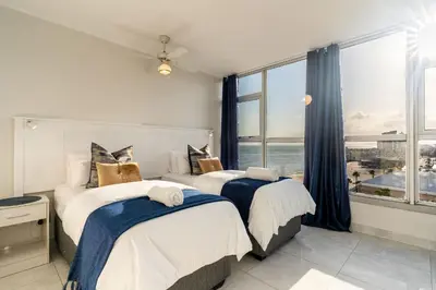 two beds in a room with a large window at Ashley on Beach Strand in Strand