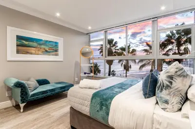 a bedroom with a large window and a bed and a chair at Ashley on Beach Strand in Strand