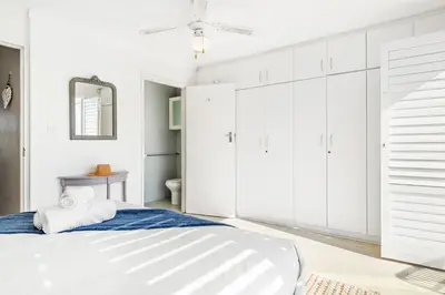 a white bedroom with a bed and a mirror at Marechale Way in Cape Town