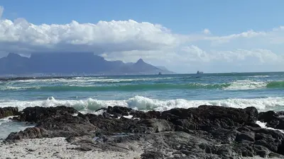 a beach with rocks and the ocean with mountains at African Holiday home in Table View in Cape Town