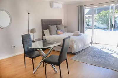a bedroom with a bed and a glass table and chairs at Pringle Nest in Cape Town