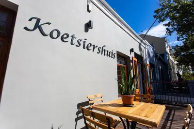 a wooden table and chairs next to a building at Koetsiershuis in Stellenbosch