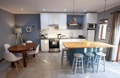 a kitchen with white cabinets and a wooden table and chairs at Culemborg Cottage in Cape Town