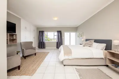 a white bedroom with a bed and a chair at Villa Eike in Grabouw