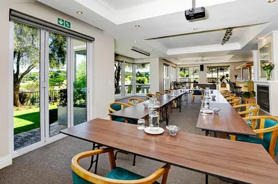a restaurant with wooden tables and chairs and windows at Bell Rosen Guest House in Bellville