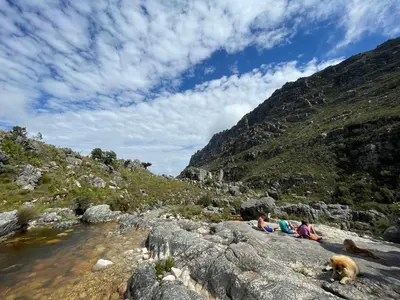 people sitting on rocks near a river with a mountain at McBains in Breerivier