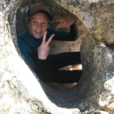 a man making a peace sign through a hole in a rock at McBains in Breerivier