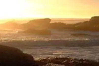 a sunset over the ocean with rocks in the water at WhiteSands in Cape Town