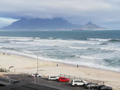 a view of a beach with cars parked next to the ocean at 504 Witsand in Bloubergstrand