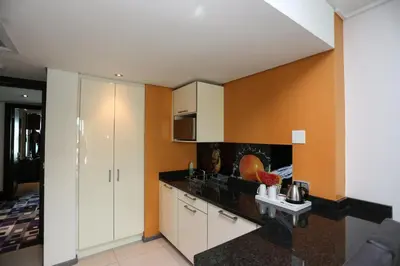 a kitchen with white cabinets and an orange wall at Hotel Verde Cape Town Airport in Matroosfontein