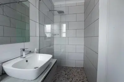 a white bathroom with a sink and a mirror at Milo's Sky Grey Guest House - No Load shedding in Cape Town