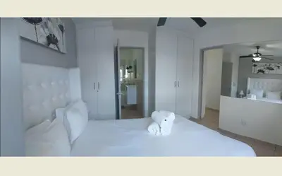a white bed with a teddy bear sitting on it at Sea Spray in Bloubergstrand