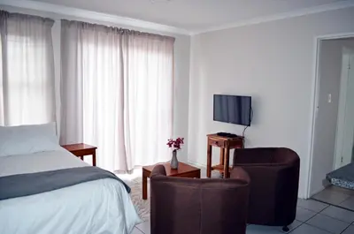 a bedroom with a bed and two chairs and a tv at Broadway Self Catering Apartments in Durbanville