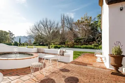a patio with a fountain and chairs on a brick patio at Cape Dutch @ Keerweder in Franschhoek