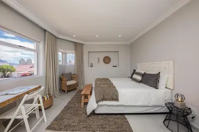 a bedroom with a bed and a desk and a window at The Little Palm in Bloubergstrand