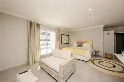 a bedroom with a bed and a couch and a chair at The Little Palm in Bloubergstrand