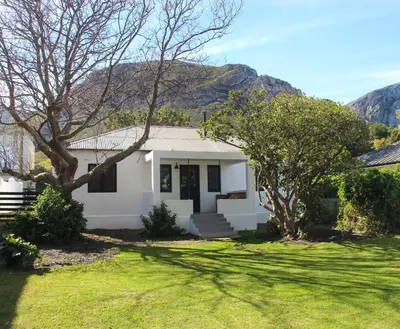 a white house with trees and mountains in the background at Langbaai Beach Cottage in Hermanus