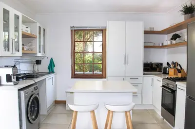 a kitchen with white cabinets and a table and stools at Langbaai Beach Cottage in Hermanus