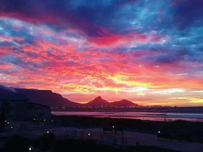a sunset over the water with mountains in the background at Lagoon Beach Neptune Isle Cape Town in Cape Town
