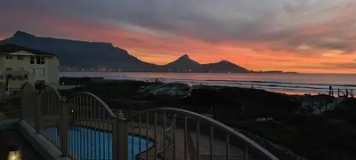 a sunset with a view of the ocean and mountains at Lagoon Beach Neptune Isle Cape Town in Cape Town