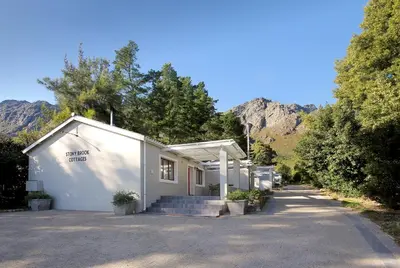 a white building with trees and mountains in the background at Stony Brook Cottages in Franschhoek